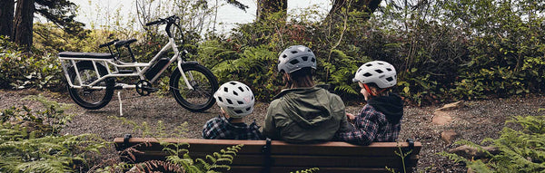 A woman and her kids sit on a rural trail alongside a RadWagon electric cargo bike.