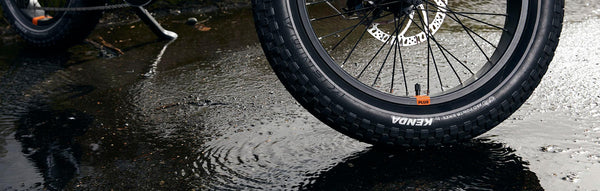 A close-up of an electric bike's fat tire on a rainy street.