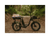 A black ebike on a dirt trail in a forest with a small basket on the front and wood and a blanket tied to the rear passenger seat.
