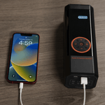 A cell phone is connected to the Rad Portable Tire Inflator and is charging via a white USB cable.