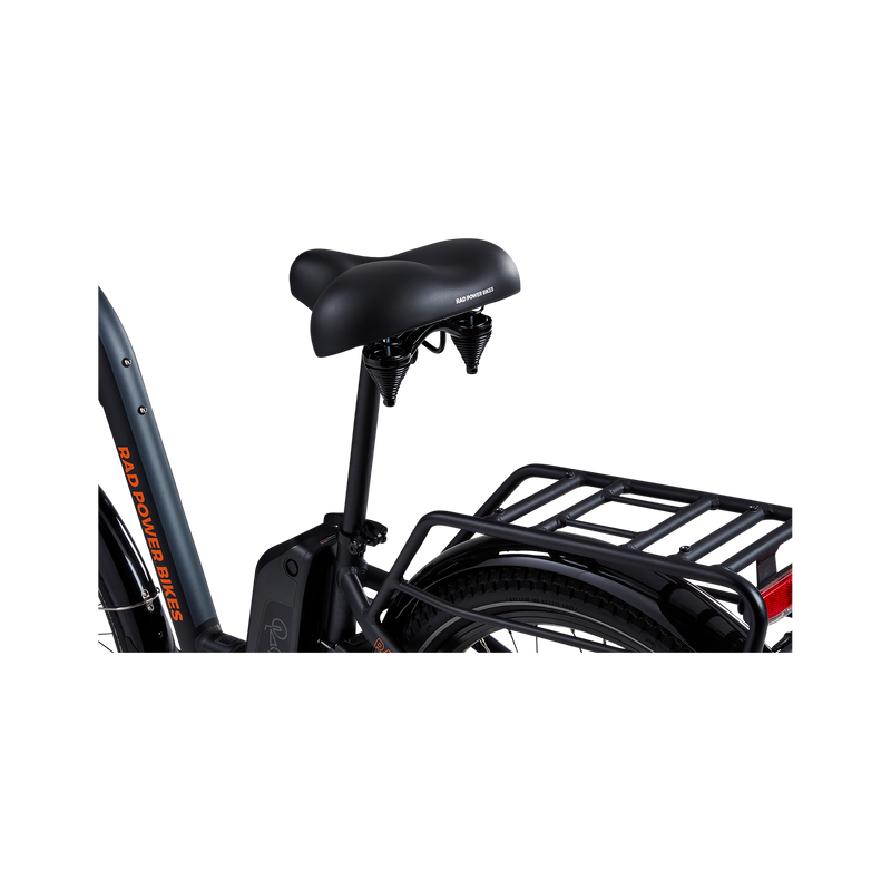 A close-up view of a grey Rad Power bike showing the side and rear of a matte black Enhanced Comfort Saddle, including the springs below the rear of the saddle