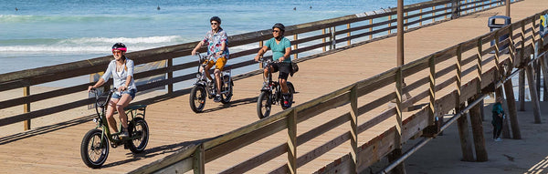 Three individuals ride their Rad Power Bikes across a bridge.