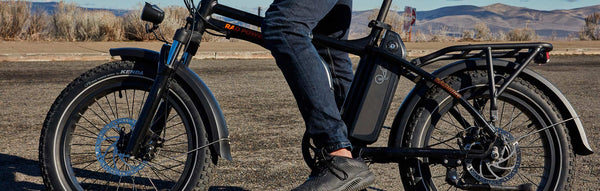 A man stands over his RadMini folding bike on a rural highway.