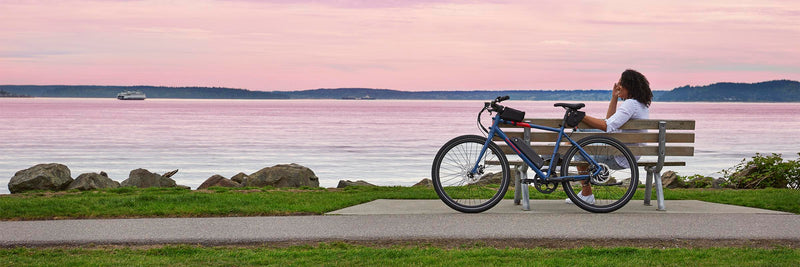 A woman sits alongside her RadMission on the waterfront at dusk.