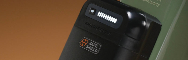 A close-up of the Safe Shield Battery on a green ebike against a brown studio backdrop.