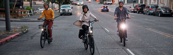 3 friends riding a RadCity 5 Plus electric commuter bike through a city at dusk.