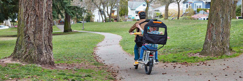 A father and children ride through a park on a RadWagon with a Conestoga 
