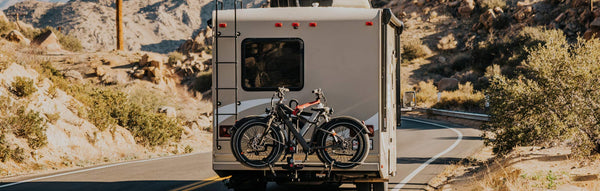 An RV rides down a rural stretch of road with two ebikes on a rack in the back.