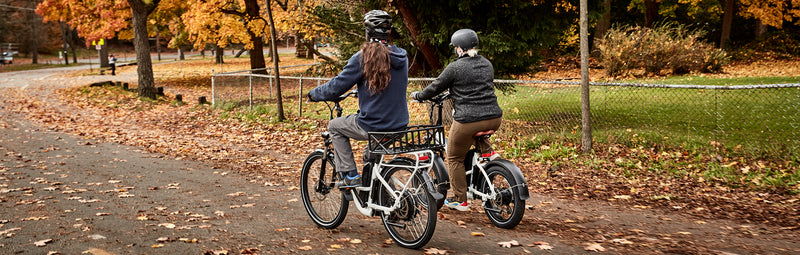 Two friends ride electric bikes from Rad Power Bikes amid fall leaves.