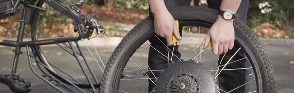 A rider stands next to his electric bike while fixing a flat tire.