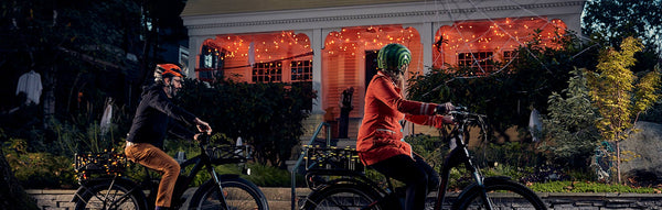 A family rides their electric bikes by a house decorated for Halloween.