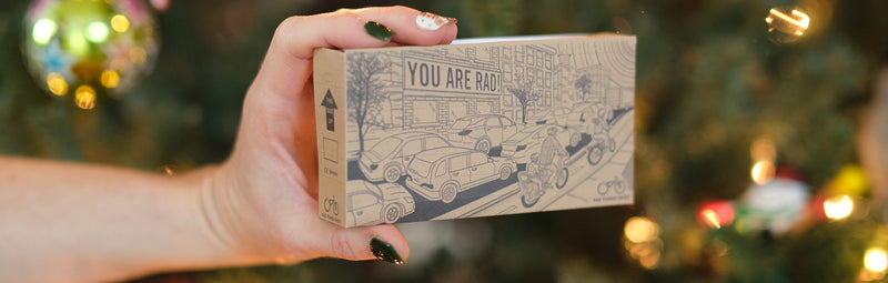 A palm-sized replica of Rad Power Bikes' cardboard ebike box held in front of a Christmas tree.