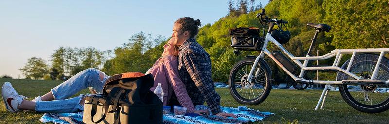 A man and woman sit on a picnic blanket alongside a RadWagon at dusk.