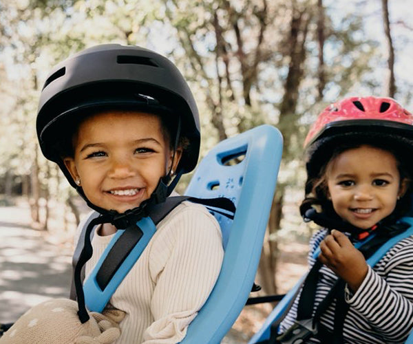 Two small children in bike helmets sitting in child seats