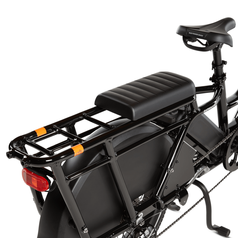 RadWagon deckpad installed in the front-most position on the back of a RadWagon electric cargo bike, used for passenger seating. Black vinyl material with padding. Subtle Rad Power Bikes logo along the end.