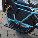 Man riding a blue RadWagon 5 electric cargo bike with two children as passengers. The children are seated with passenger accessories including the RadWagon 5 Deckpad, RadWagon 5 Running Boards, an orange thule yepp child seat and a caboose.
