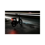 Photo of a Rad Power Bikes RadRunner electric cargo bike with passenger package parked at night on a damp street with Rad logo taillight turned on and mounted below rear seat on the rack.