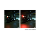 Distance photo of the rear of a Rad Power Bikes RadRunner electric cargo bike with passenger package parked at night on a damp street with Rad logo taillight turned on and mounted below rear seat on the rack.