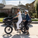 Woman riding an electric utility bike on a trail, with a passenger package installed where a second rider could ride.