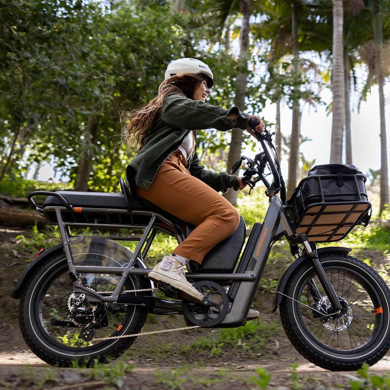 Woman riding an electric utility bike on a trail, with a passenger package installed where a second rider could ride.