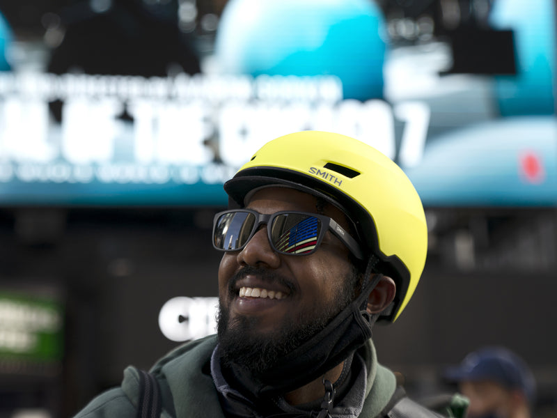 A person wearing sunglasses and a neon yellow Smith Express MIPS helmet