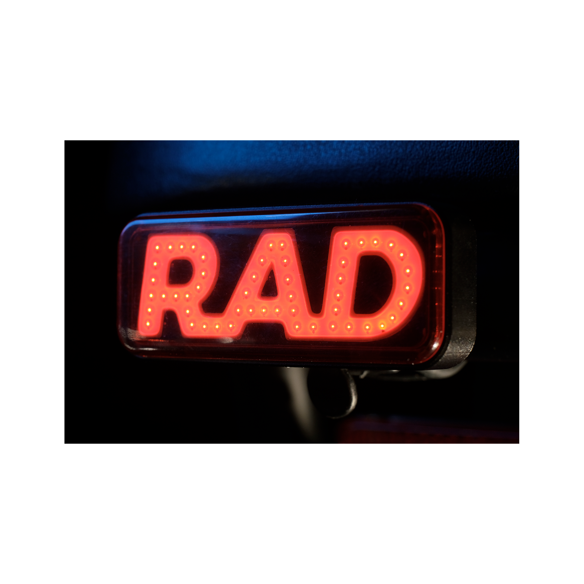 Close up photo of Rad Power Bikes Rad Logo taillight mounted on a bicycle at night with light turned on.