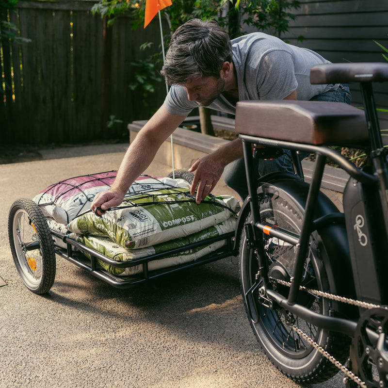 A man securing the cargo net over bags of compost on the Rad Trailer, attached to an electric cargo bike.